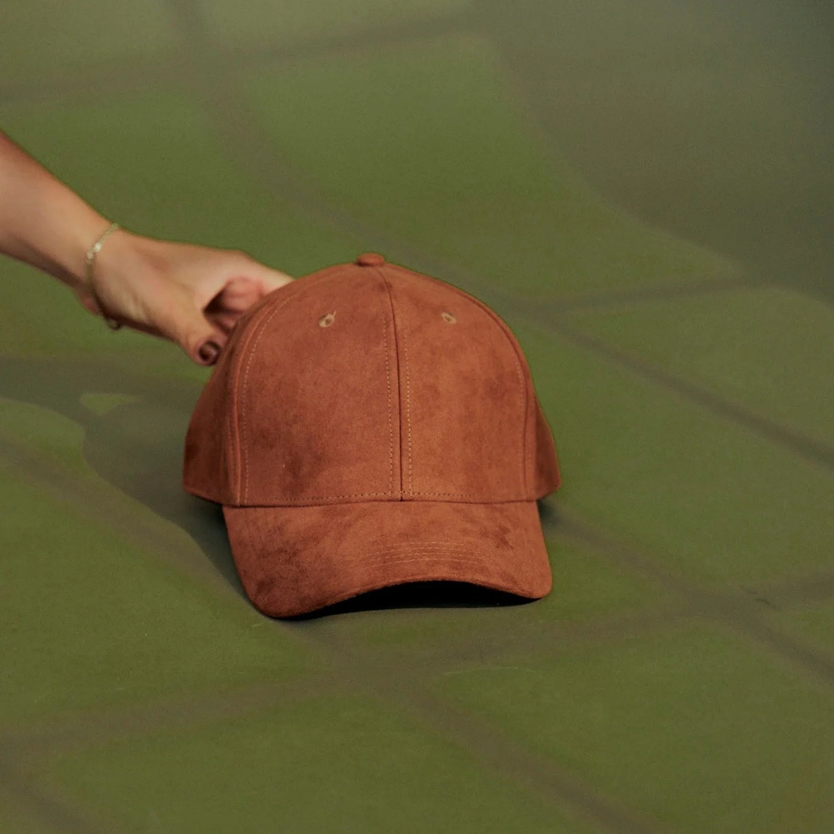 Brown suede cap held by a hand on a green surface